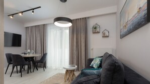 A modern living room with a dark sofa, a round coffee table, and a dining area with chairs and a table. - Cozy Apartment | Close to Beach and Lake, Parking. (Mielno)