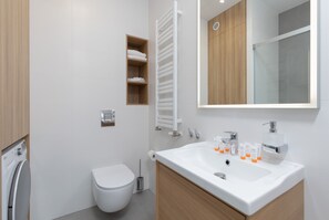 A modern bathroom with a white sink, wooden cabinets, a toilet, a towel rack, and a mirror.