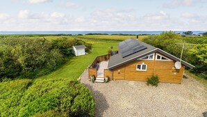 A wooden house with a gravel driveway, a small shed, and a view of the sea. - Stunning home in Vestervig with sauna (Vestervig)