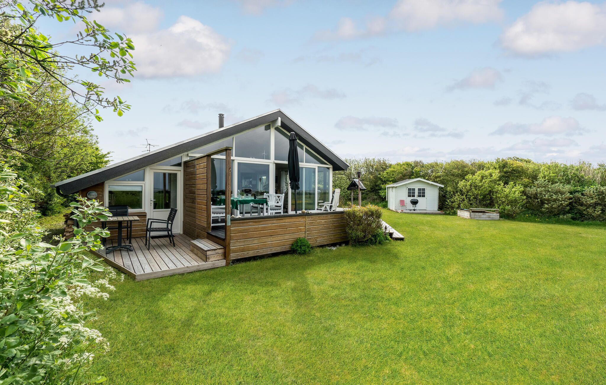 Een modern huis met een terras, een tuinhuisje en een gazon.
