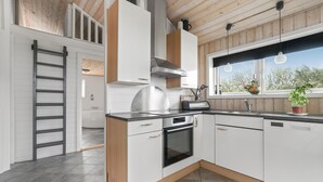 A modern kitchen with white cabinets, a stainless steel range hood, and a window with a view of trees. - Stunning home in Vestervig with sauna (Vestervig)