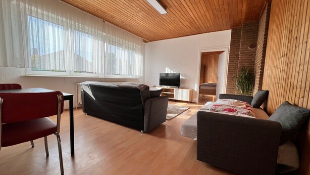Un salon moderne avec un plafond en bois, un canapé, un téléviseur et un mur en briques.