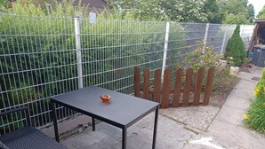 Un espace patio avec une table en métal et deux chaises, entouré d’une clôture en métal et d’une clôture en bois à lattes.