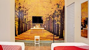 Habitación de hotel con dos camas, un televisor en la pared y un mural de un sendero boscoso.