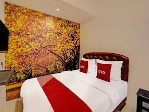 Une chambre d’hôtel avec un lit, une literie rouge et blanche, une tête de lit rouge et une grande fresque murale représentant des feuilles d’automne.