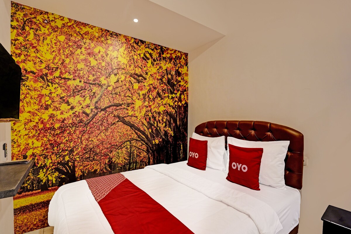 A hotel room with a large bed, red and white bedding, and a wall mural of autumn leaves.
