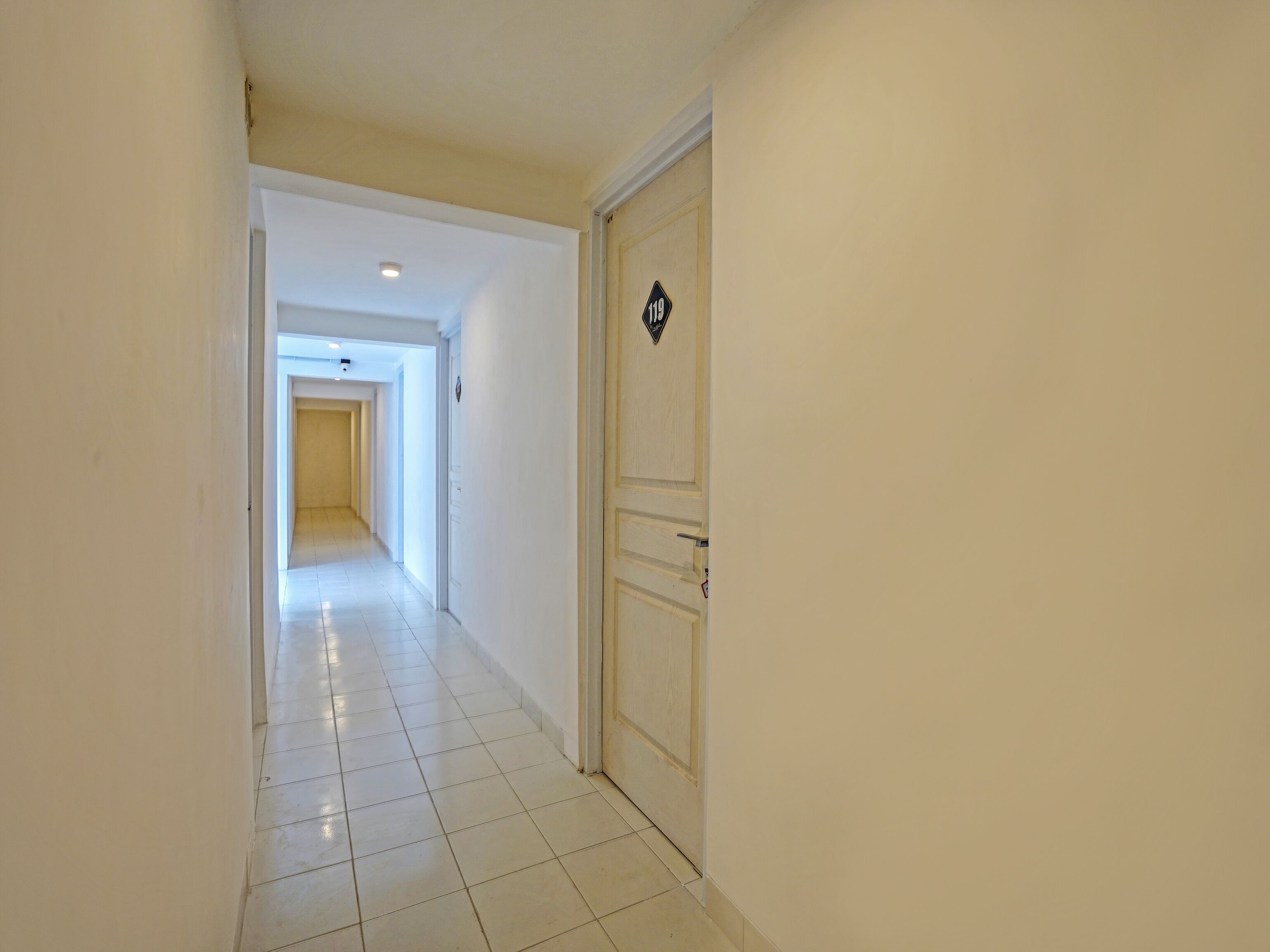 A hallway with white walls and a tiled floor leading to a door marked with the number 119.