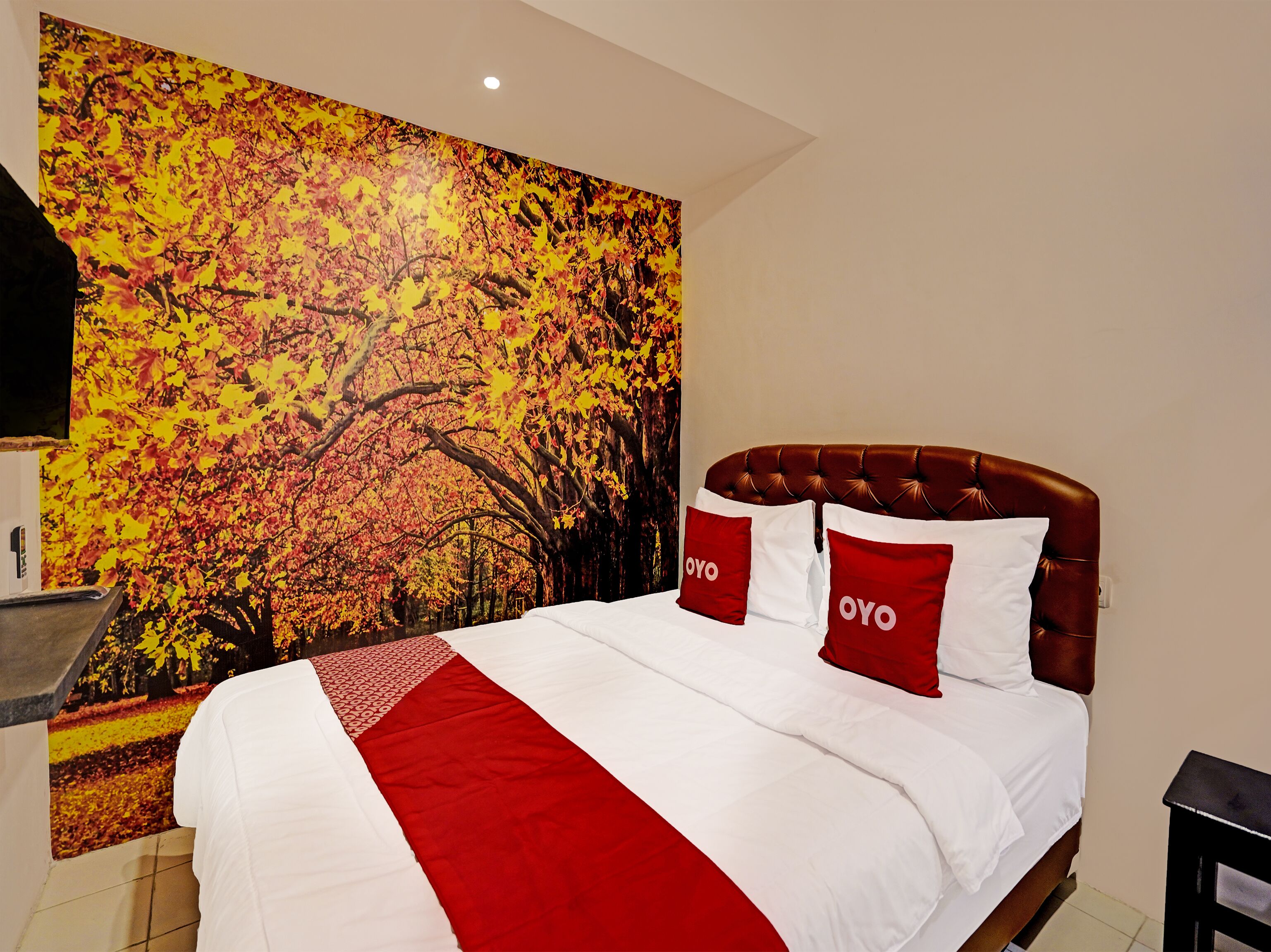 Una habitación de hotel con una cama grande, ropa de cama roja y blanca, y un mural en la pared con hojas de otoño.
