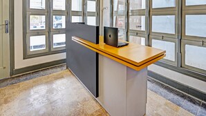 Un mostrador de recepción con una computadora portátil, ventanas amplias y piso de baldosas.