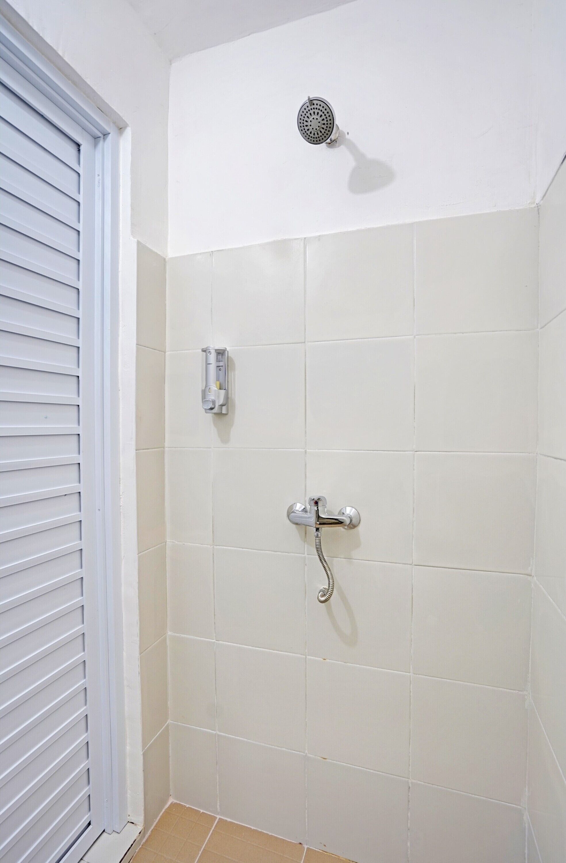 A bathroom with white tiles, a showerhead, and a handheld shower attachment.