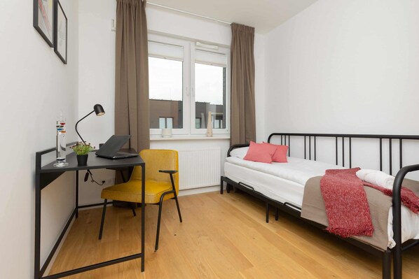 A compact room with a bed, a desk, a chair, and a window with curtains.