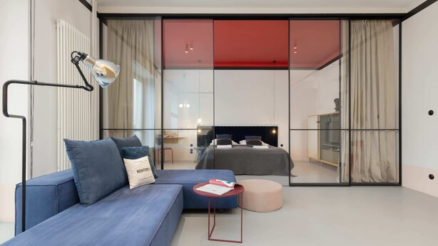 Une chambre moderne avec un grand lit, un canapé bleu, une petite table et une cloison en verre.