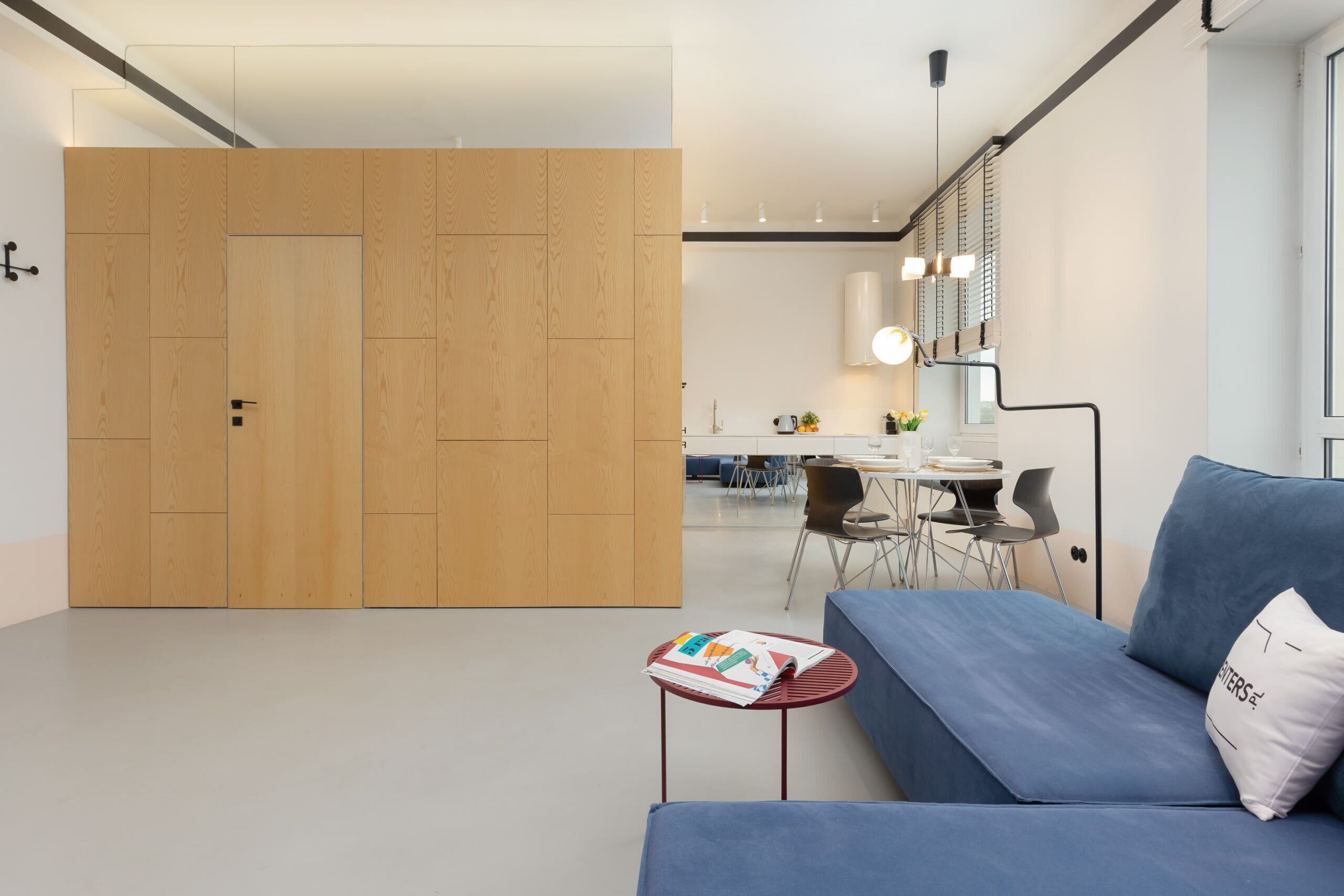 Un salon moderne avec un canapé bleu, une petite table avec des magazines et un mur de séparation en bois.