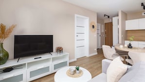 A modern living room with a flat-screen TV, white furniture, and a dining area with a round table. - Comfortable Apartment | Balcony | Parking | Close to Park (Swinoujscie)