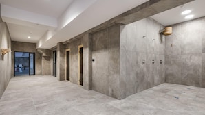 Ein moderner Flur mit grauen Fliesenböden und -wänden, mit einer Holztür und einem kleinen Holz-Eimer an der Wand.