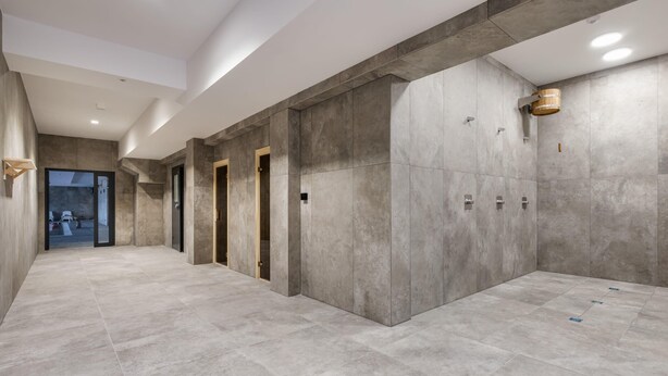 A modern hallway with grey tiled floors and walls, featuring a wooden door and a small wooden bucket on the wall. - Prestigious Apartment | Jacuzzi and Balcony (Dziwnów)