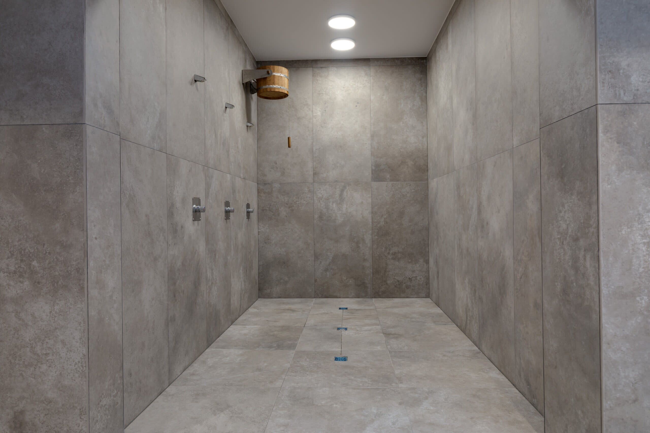 Um espaço de chuveiro estreito revestido com azulejos, com um balde de madeira e uma pequena prateleira.