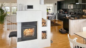 Una sala de estar moderna con chimenea, un comedor y una cocina con armarios oscuros y un microondas de acero inoxidable.