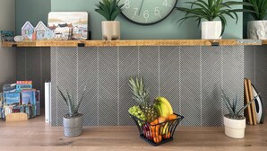 Una cocina con un reloj, una cesta de fruta y una planta en maceta sobre el mostrador.