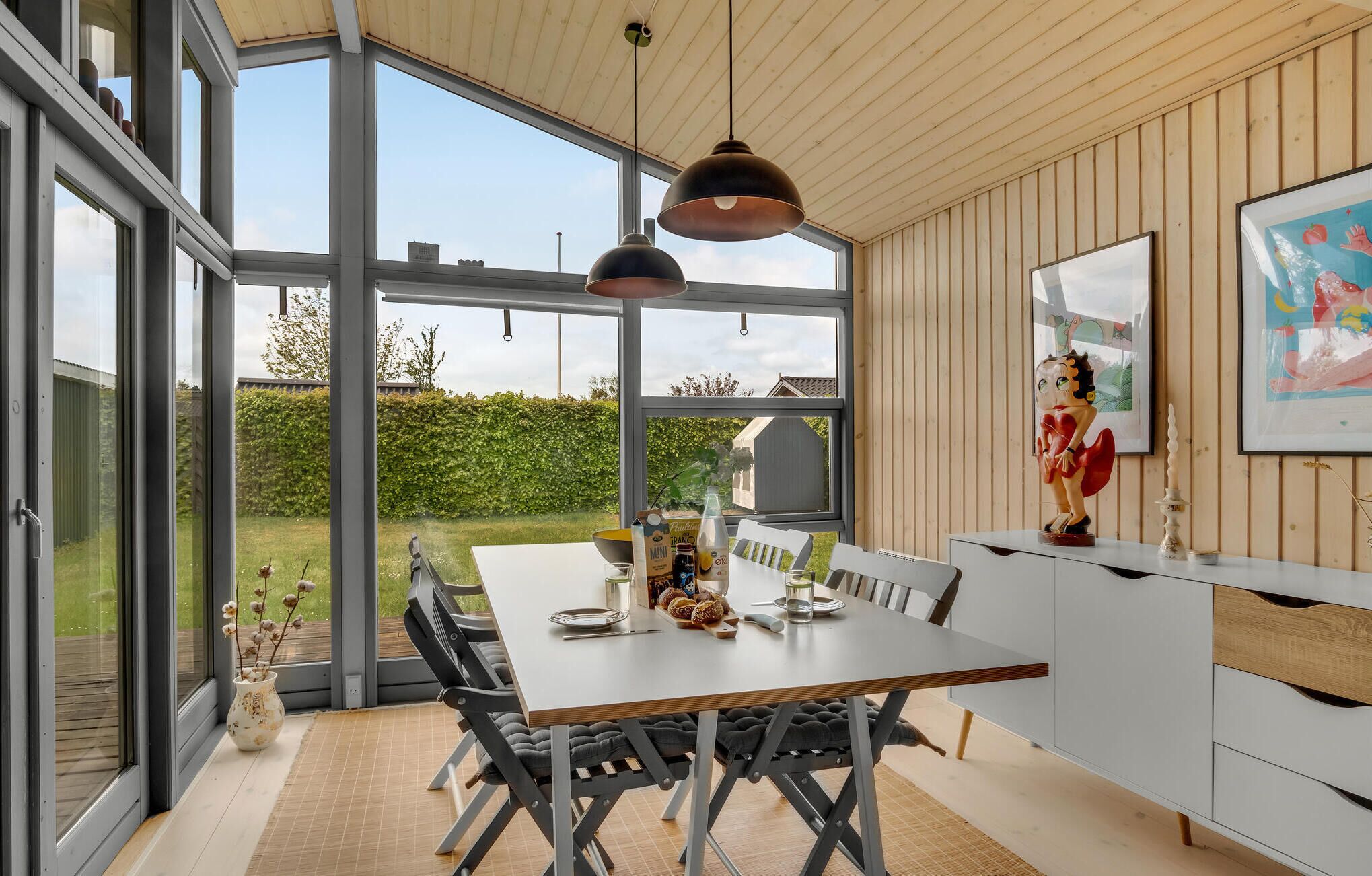 Une cuisine moderne dotée d’une grande table à manger, de luminaires suspendus et offrant une vue sur le jardin.