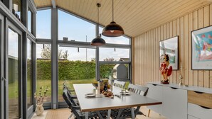 A modern kitchen with a large dining table, pendant lights, and a view of the garden.