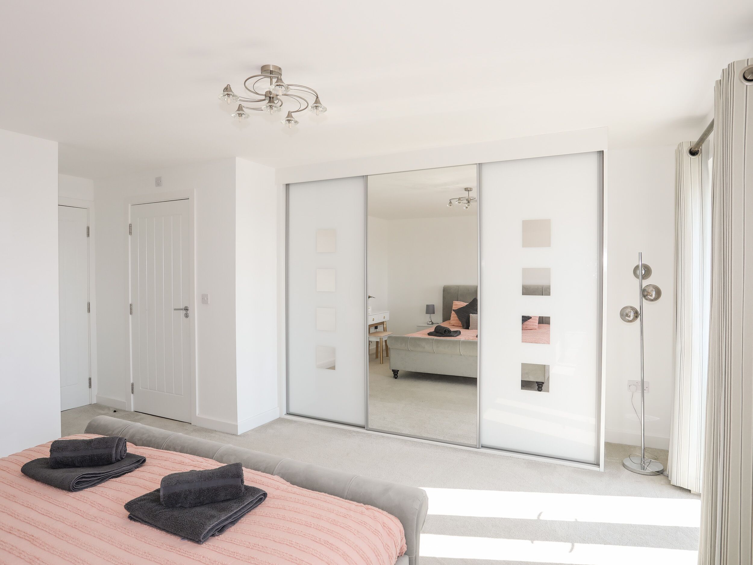 Un dormitorio moderno con una cama, un espejo grande y una puerta corrediza que da a un baño.