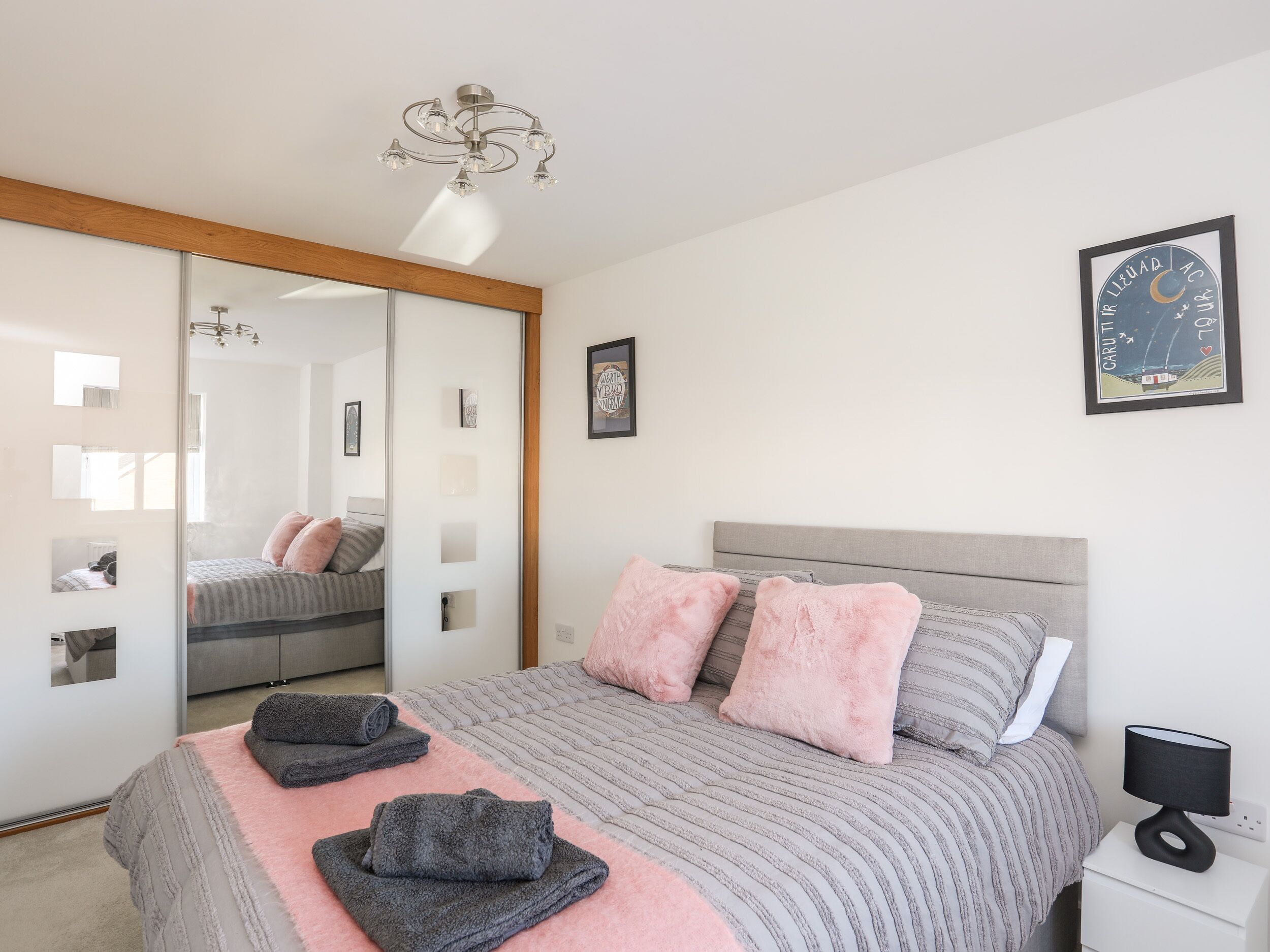 A bedroom with a bed, pillows, a bedside table with a lamp, a mirror, and a ceiling light fixture.