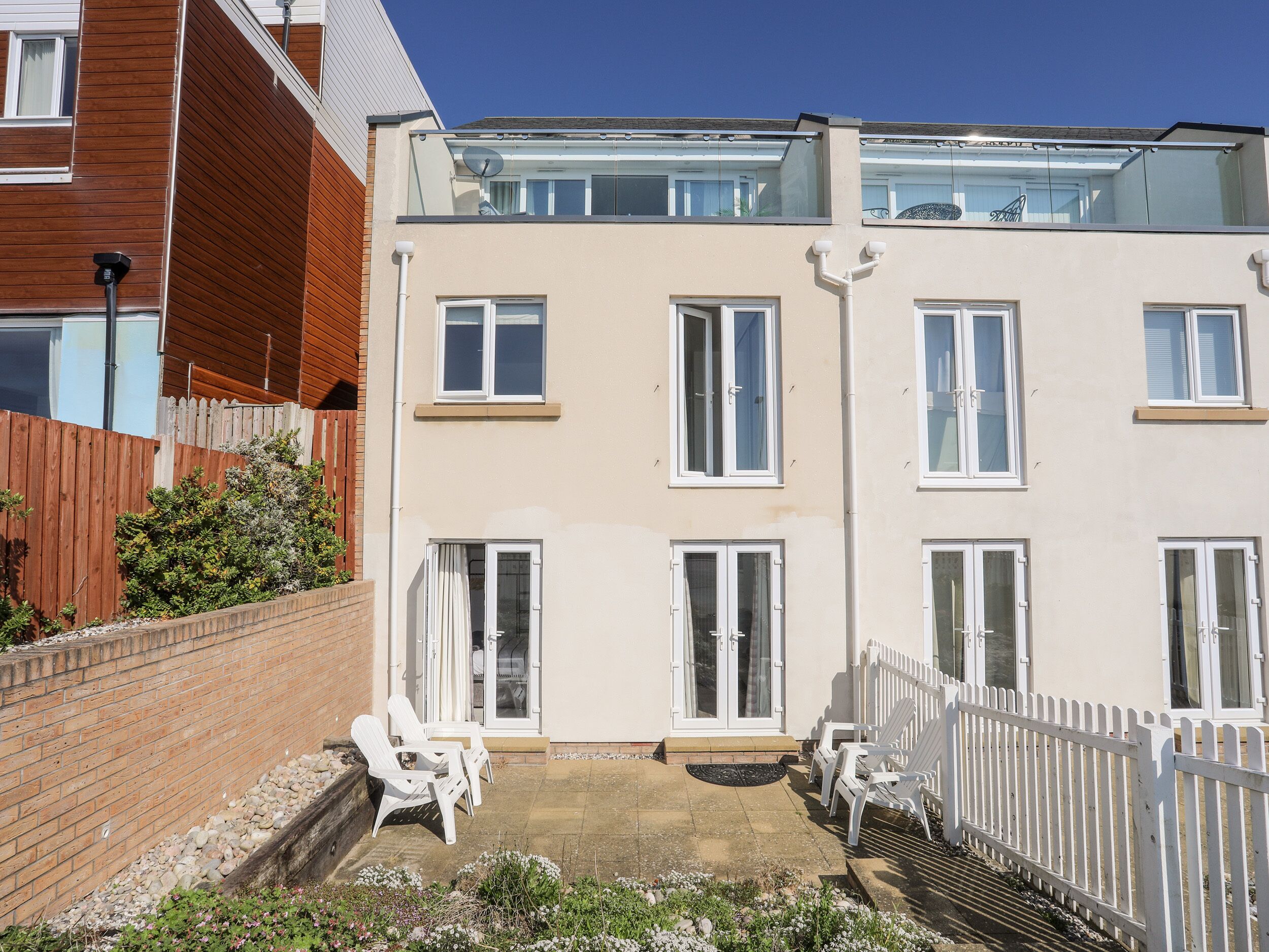 Un immeuble résidentiel de deux étages doté d’un balcon, d’un mur en briques et d’une clôture en bois peinte en blanc.