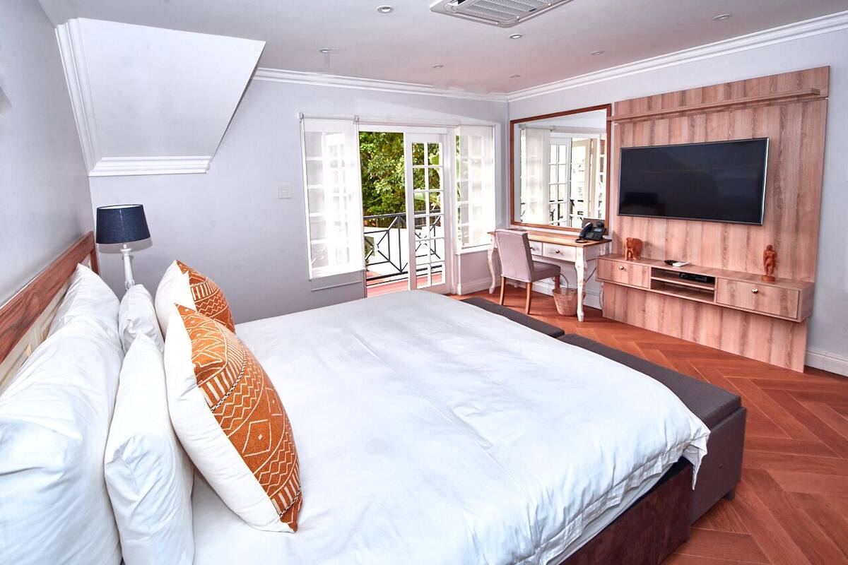 Un dormitorio con una cama grande, un escritorio, un televisor y un balcón.
