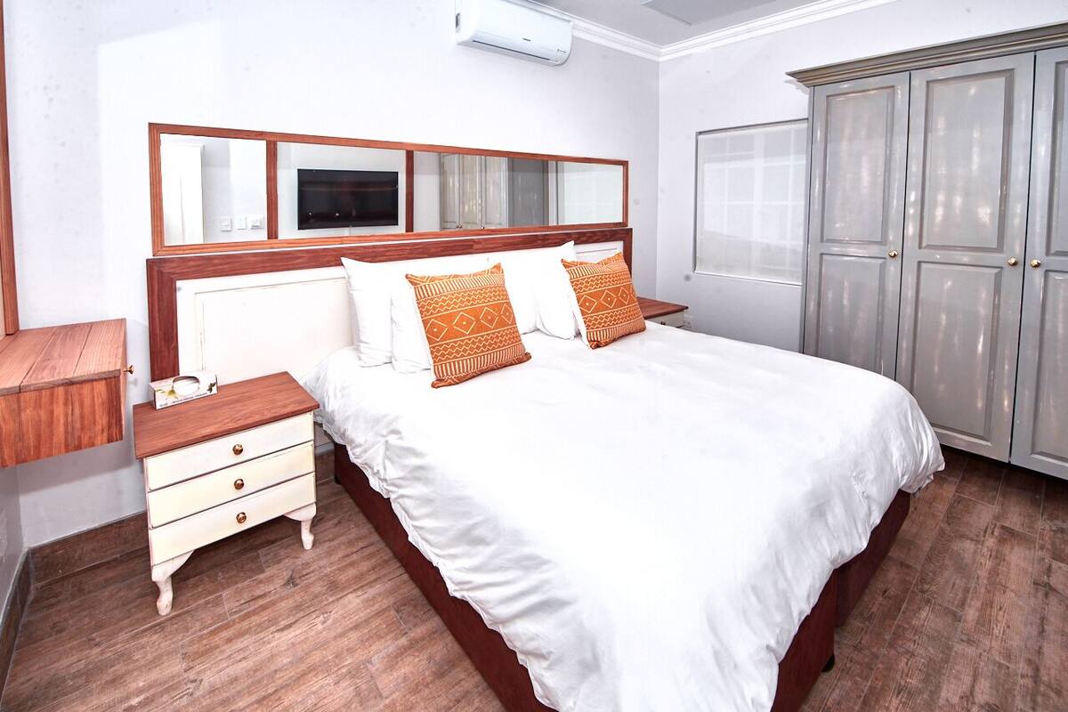 Un dormitorio ordenado con una cama grande, una mesita de noche de madera, un armario y un espejo sobre la cama.