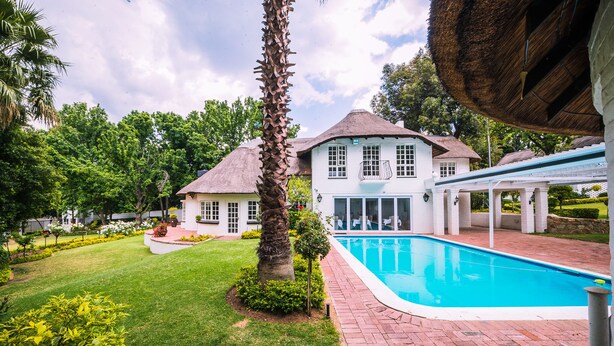 A house with a swimming pool, surrounded by a well-maintained lawn and palm trees. - Sandton Country Manor (Sandton)