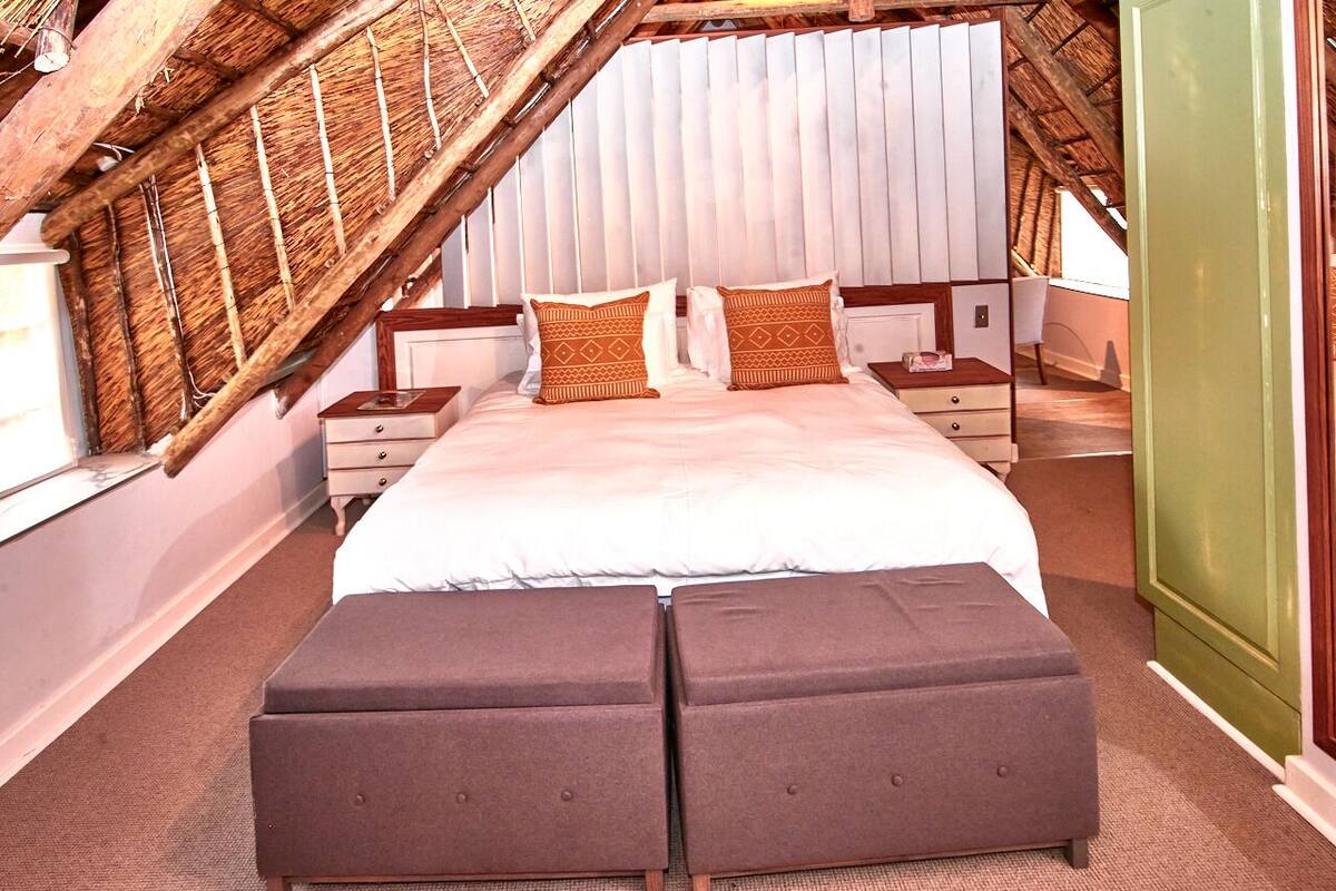Un dormitorio con techo inclinado, una cama con dos almohadas, una mesita de noche y una pared verde.