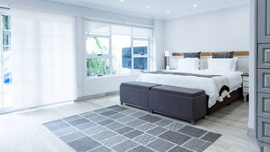 A modern bedroom with a large bed, a bedside table, and a window with a view of greenery. - Sandton Country Manor (Sandton)
