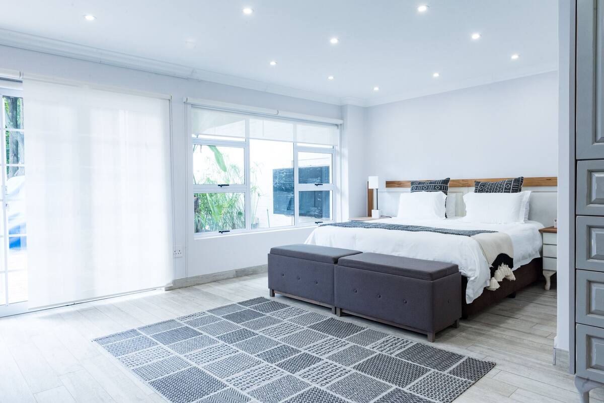 Un dormitorio moderno con una cama grande, una mesita de noche y un ventanal con vistas a zonas verdes.