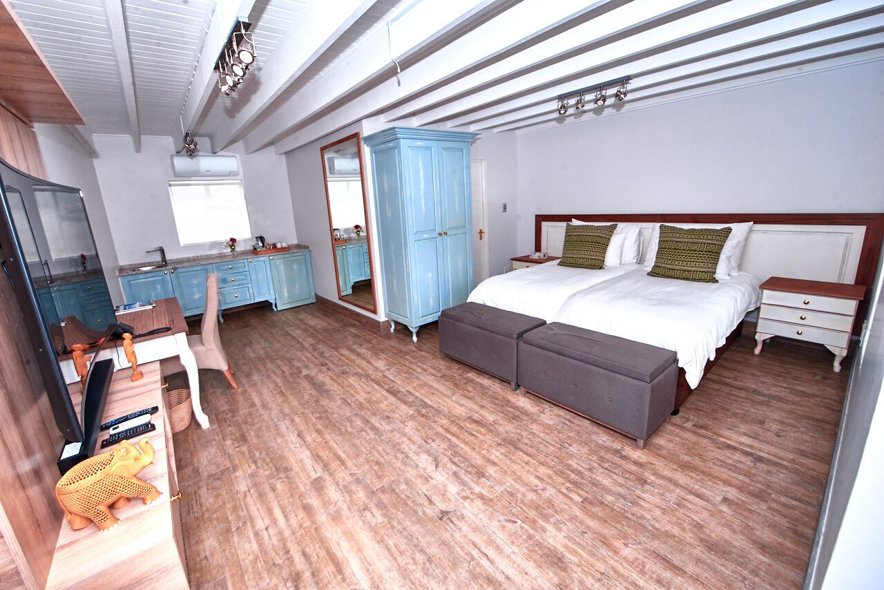 A bedroom with a wooden floor, a bed with white bedding, a blue wardrobe, a desk with a chair, and a mirror.