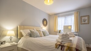 A neatly made bed with white linens and a colorful throw blanket, a bedside lamp, and a radio on a white nightstand. - The Mews -  a beautiful cottage hidden away just off the village pond.  (Goudhurst)
