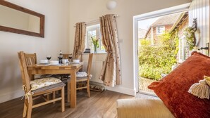 A cozy room with a wooden dining table set for two, a comfortable chair, and a red cushion. - The Mews -  a beautiful cottage hidden away just off the village pond.  (Goudhurst)