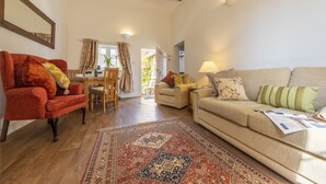 A spacious living room with a red armchair, beige sofa, wooden dining table, and a patterned rug. - The Mews -  a beautiful cottage hidden away just off the village pond.  (Goudhurst)
