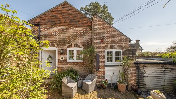A brick house with a white door, a small porch with wicker furniture, and potted plants. - The Mews -  a beautiful cottage hidden away just off the village pond.  (Goudhurst)