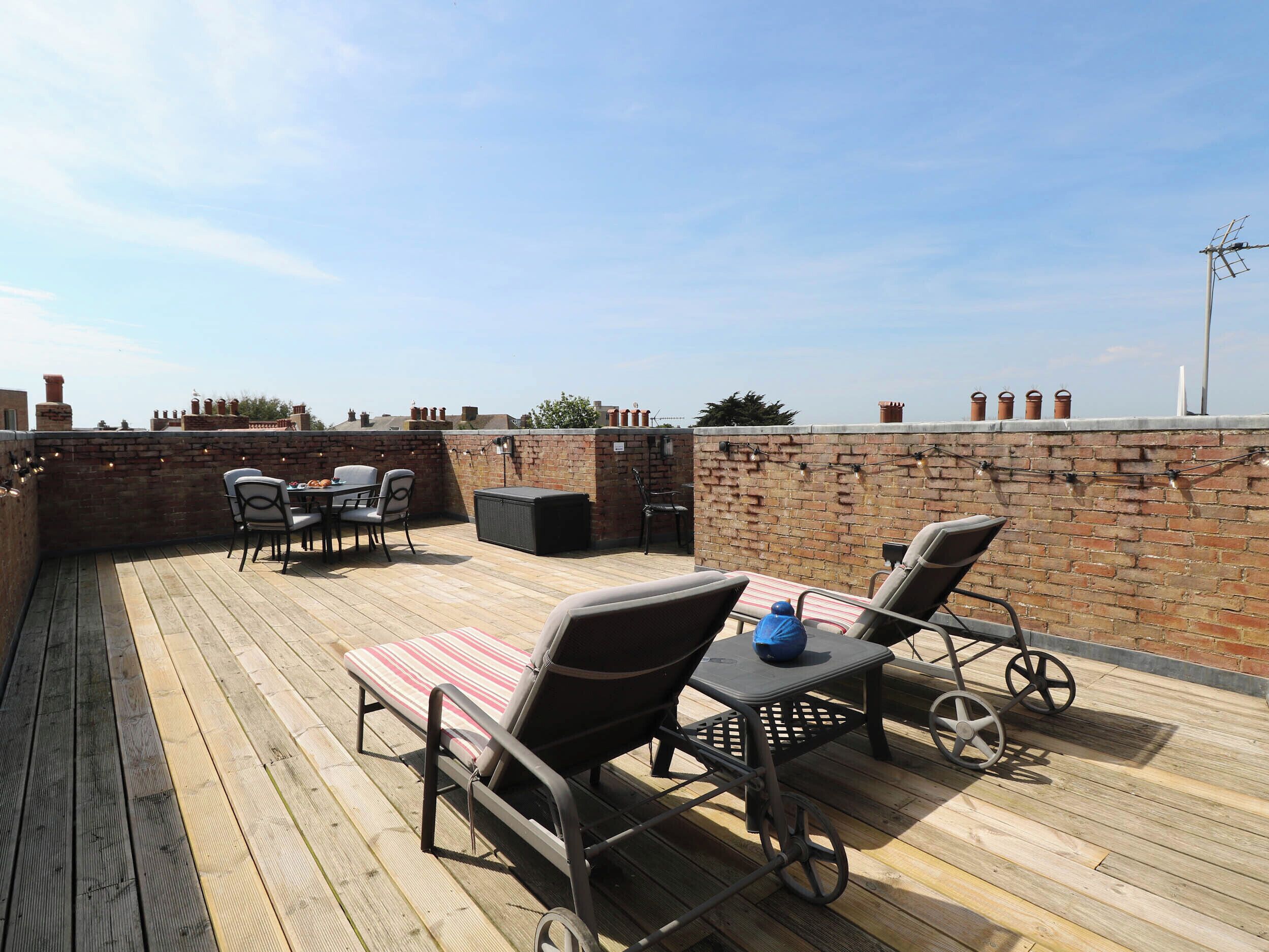 A rooftop patio with a wooden deck, outdoor seating, and a brick wall.
