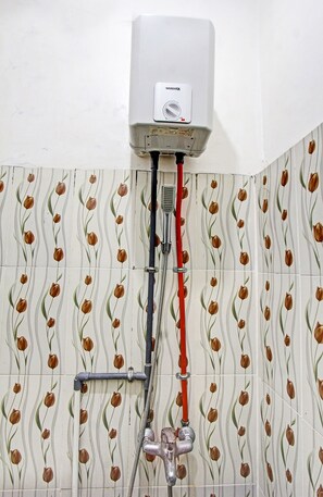 A bathroom with a wall-mounted water heater, a shower with a red hose, and patterned tiles. - OYO 3741 Mutiara Syariah 1 (Mataram)