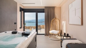 A modern hotel room with a large bed, a small sofa, a wicker chair, a balcony with a view of the sea, and a hot tub. - Villa Ponti (Novigrad)