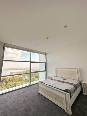 A bedroom with a large window, a bed with a glass headboard, and a small bedside table.
