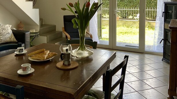 A dining area with a table set for two, a vase with flowers, and a view of the garden through glass doors. - The Sisters' house (Santo Stefano di Magra)