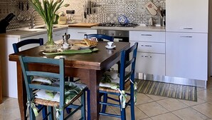 A modern kitchen with white cabinets, a tiled backsplash, and a dining area with a wooden table and blue chairs. - The Sisters' house (Santo Stefano di Magra)