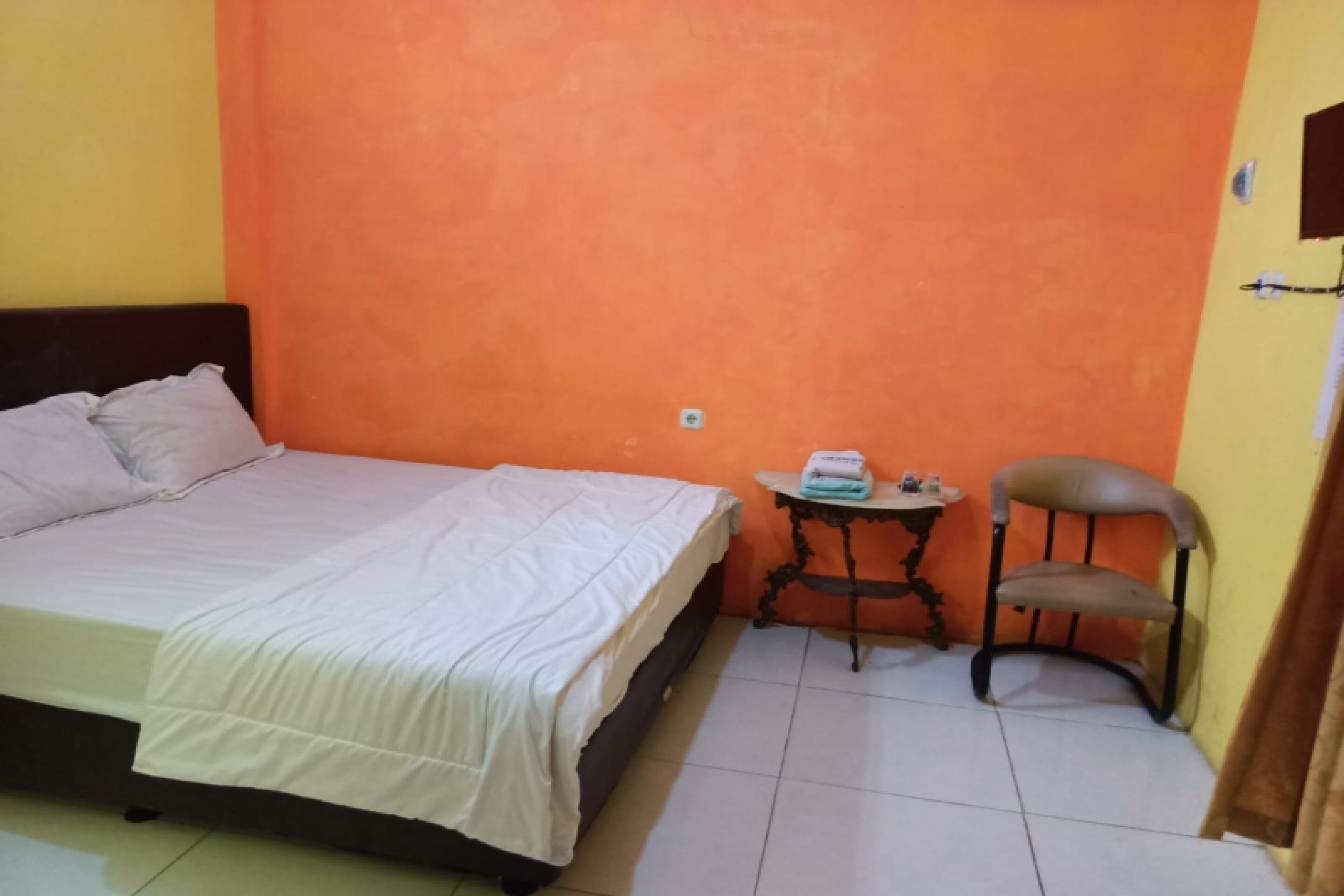 Un dormitorio pequeño y ordenado con una cama, una mesita con una silla y un estante en la pared.