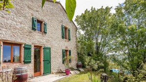 A stone house with green shutters, a wooden door, and a small garden with a potted plant and a barrel. - Le Triangle D'or - Gite 80m2 - Piscine - Gaillac (Gaillac)