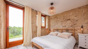 A bedroom with a wooden bed, a nightstand, a window with curtains, and a stone wall. - Le Triangle D'or - Gite 80m2 - Piscine - Gaillac (Gaillac)