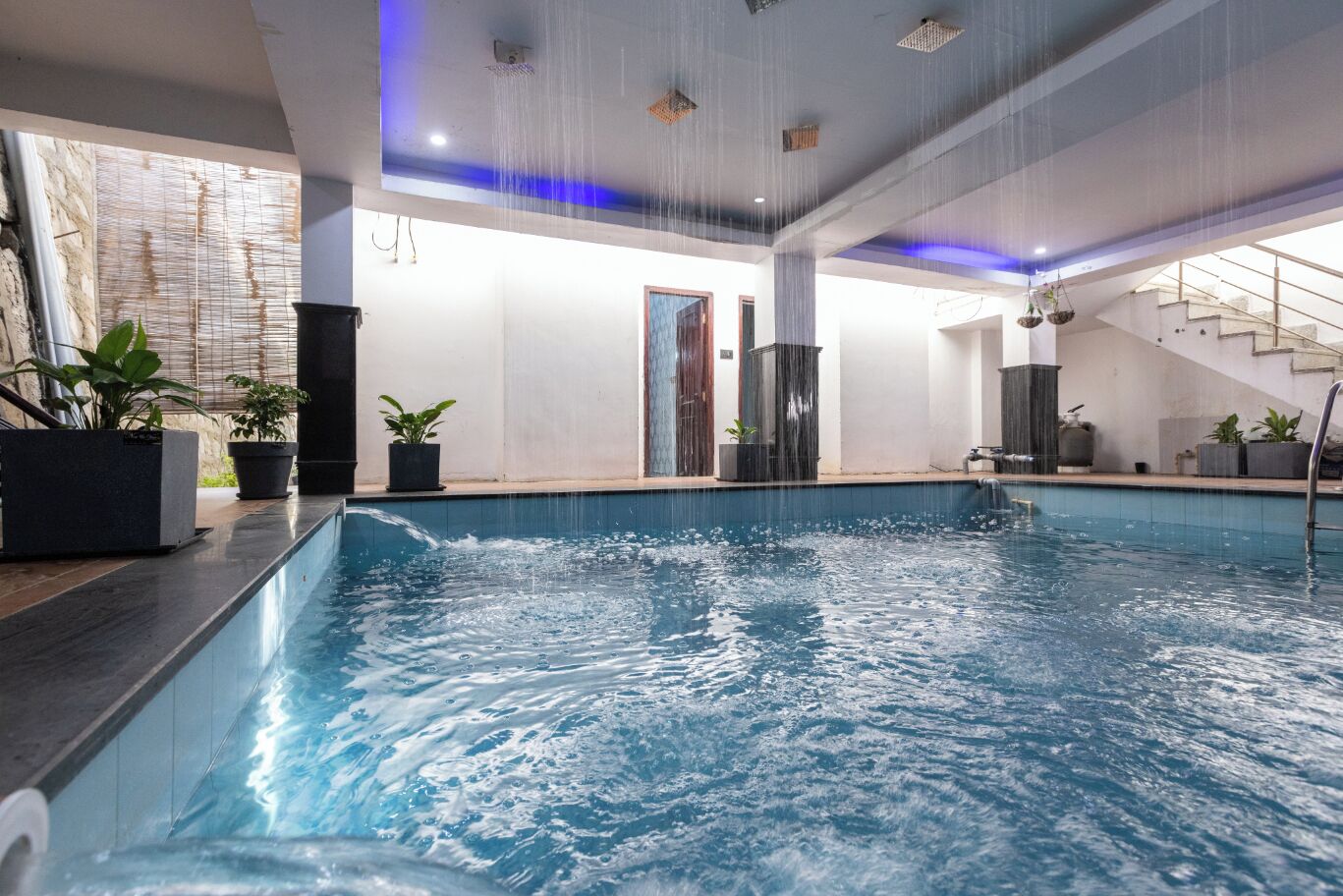 An indoor swimming pool with a modern design, including a glass ceiling and a staircase leading to an upper level.