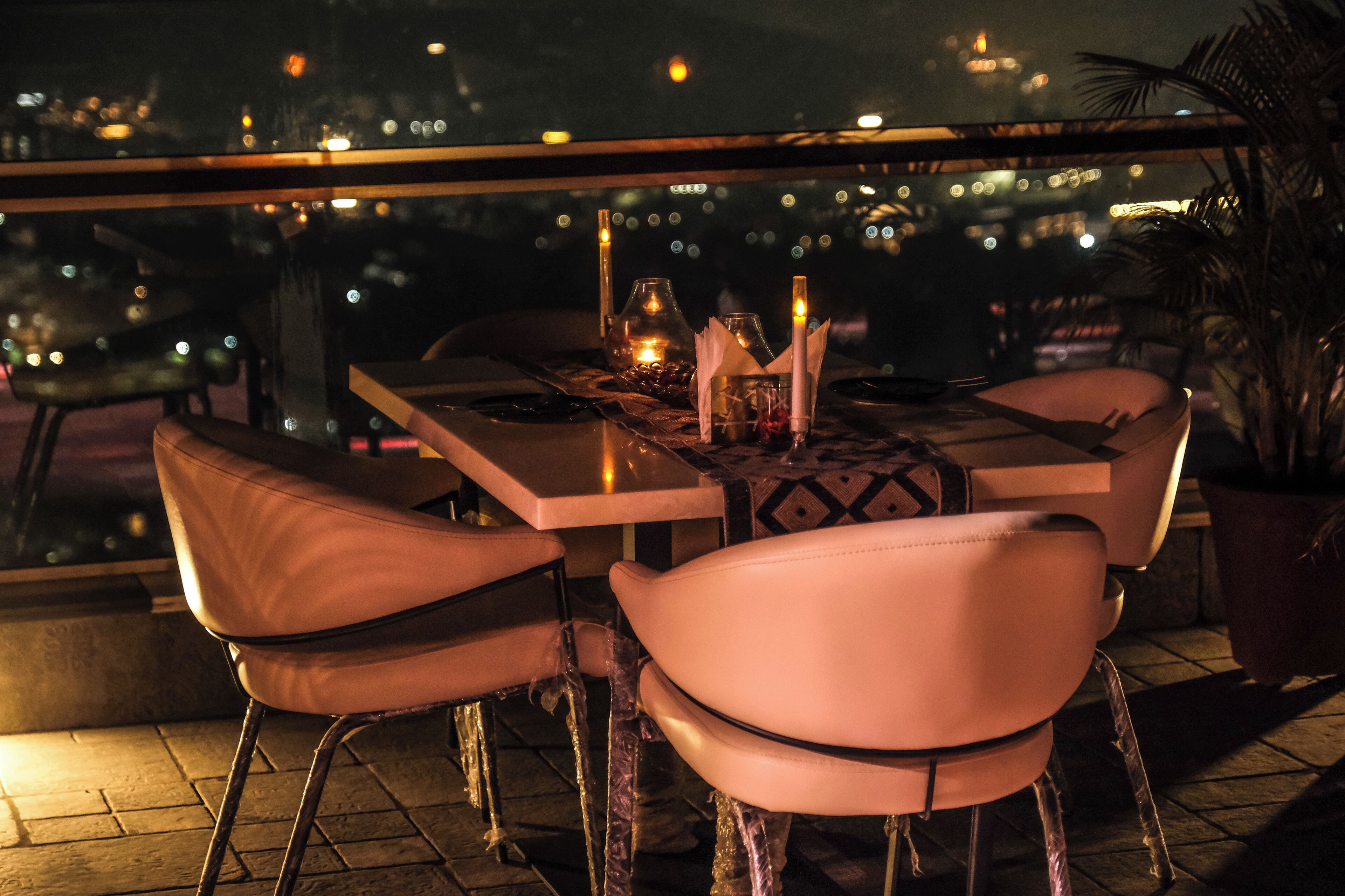 A restaurant with a table set for two, chairs, and a view of the cityscape at night.